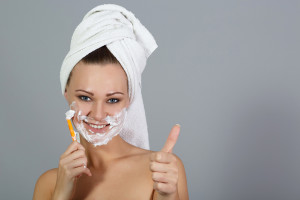 Girl shaving face and shows thumbs up at grey background