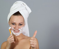 Girl shaving face and shows thumbs up at grey background